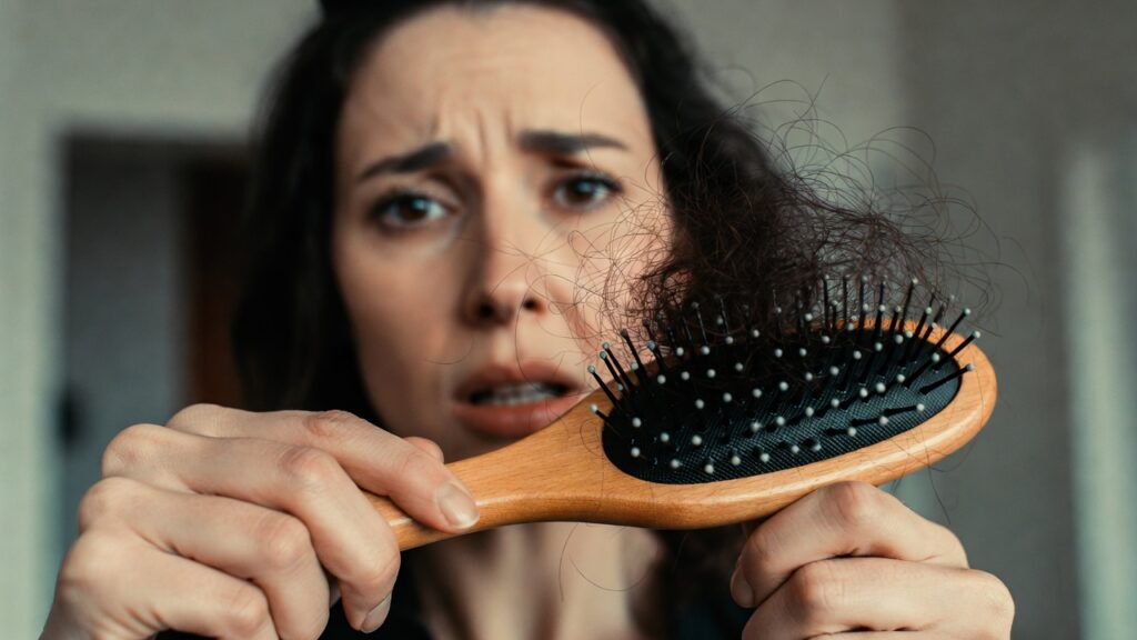 Mulher preocupada segurando uma escova cheia de fios soltos, tentando descobrir se o cabelo está caindo ou quebrando